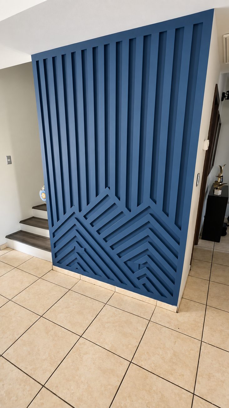 Blue painted slat wall above a mitred chevron pattern panel, dividing an entry from a staircase