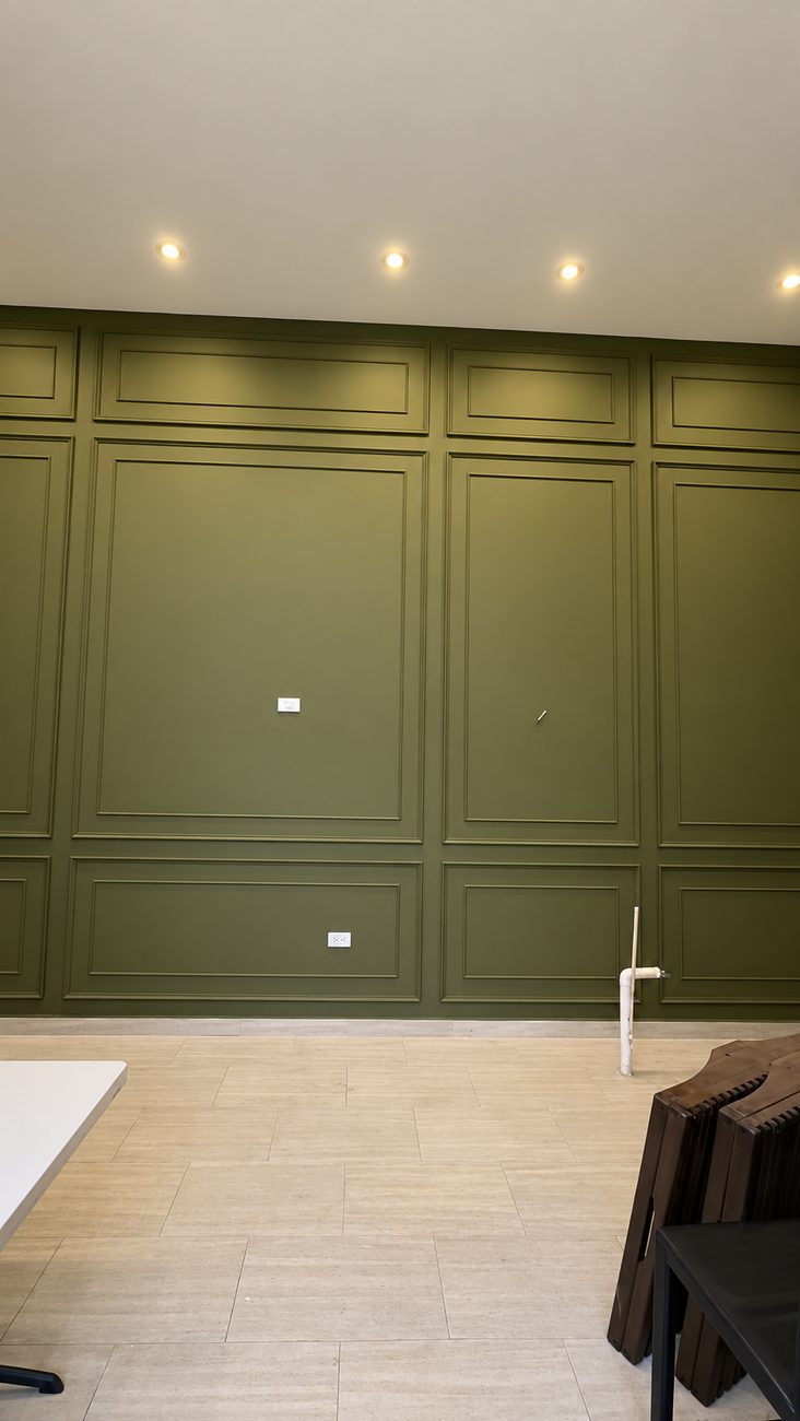 Olive green accent wall with applied picture-frame moulding lit by recessed downlights