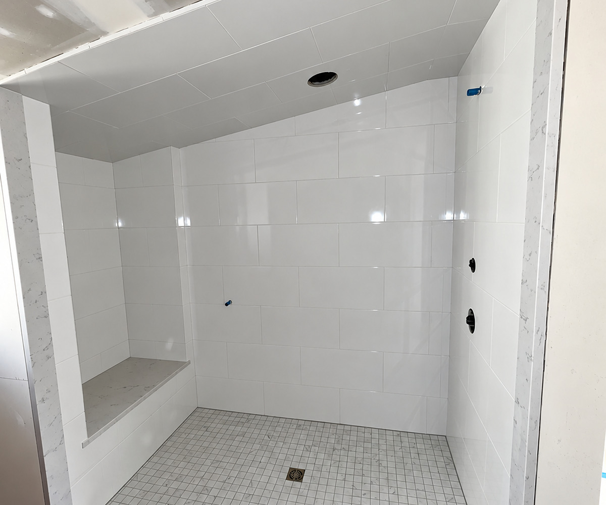 The same walk-in shower finished in large white tile, with a built-in bench, marble-look jambs and a mosaic pan draining to the centre
