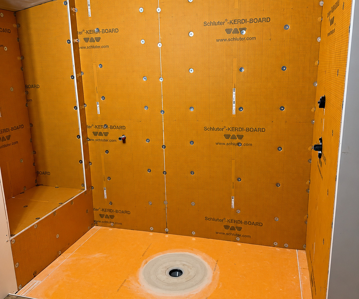 Walk-in shower enclosure built in orange Schluter KERDI-BOARD panels, with a built-in bench, valve outlets and a sloped pan draining to a bonding flange