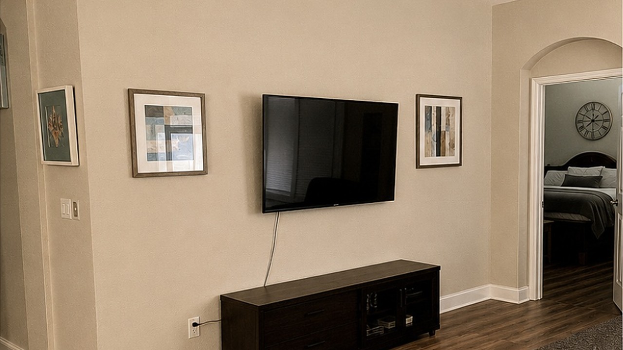 Plain living room wall with a wall-mounted TV, visible cable and a low timber console
