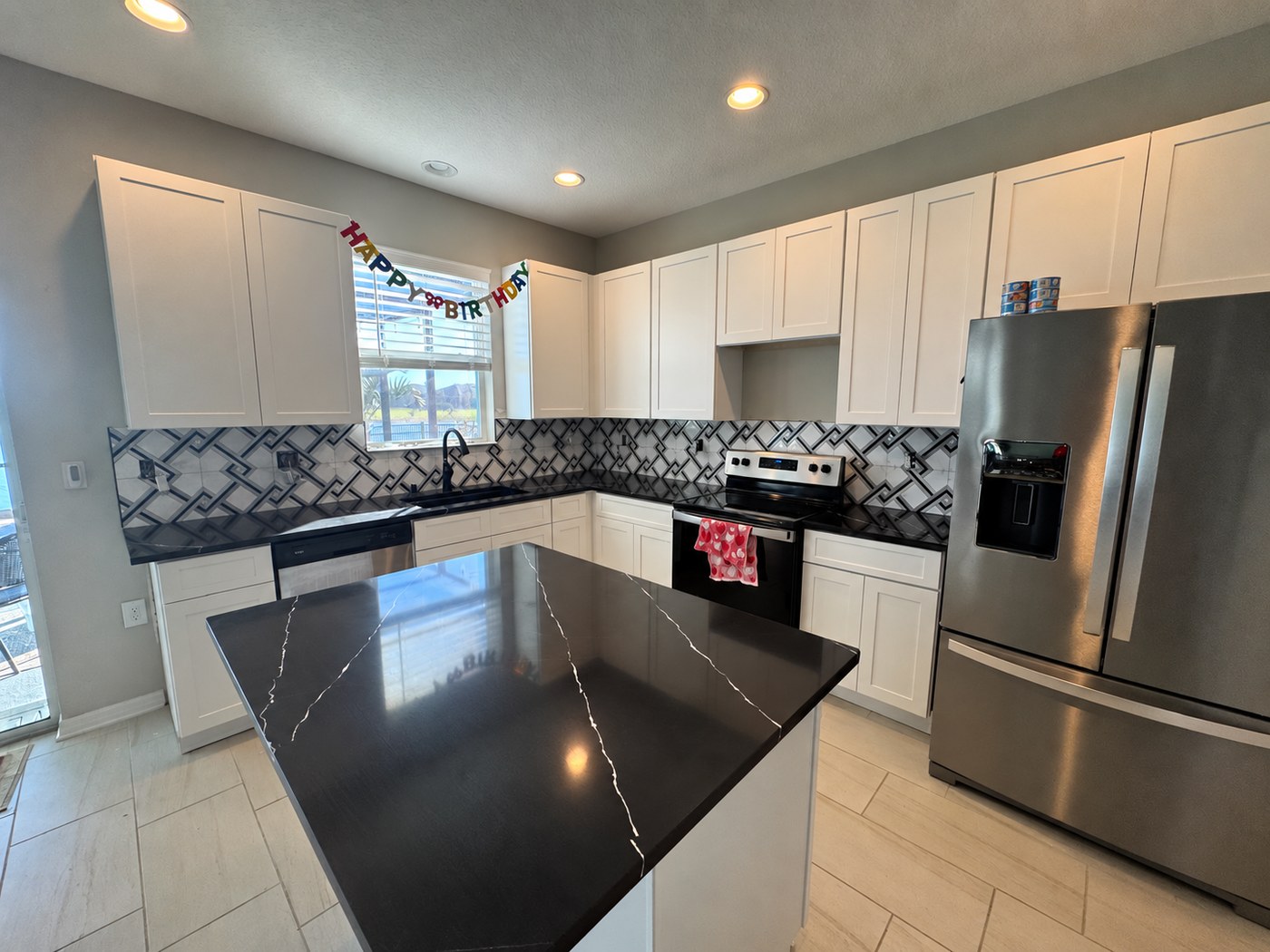 Remodelled kitchen with white shaker cabinets, black veined quartz counters, a long island and a black and white geometric tile backsplash