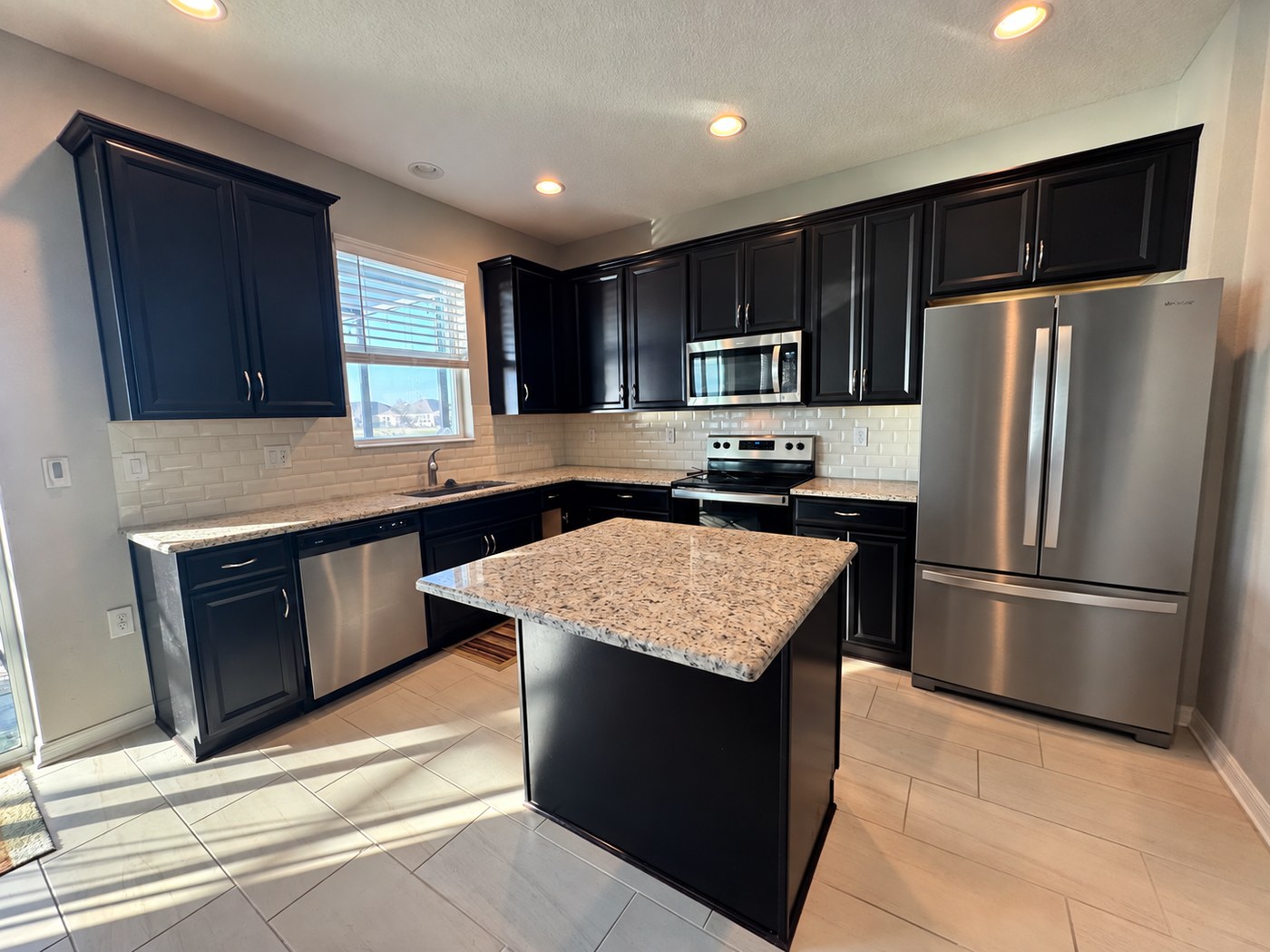 Kitchen with dark brown raised-panel cabinets, beige speckled granite counters and a small square island