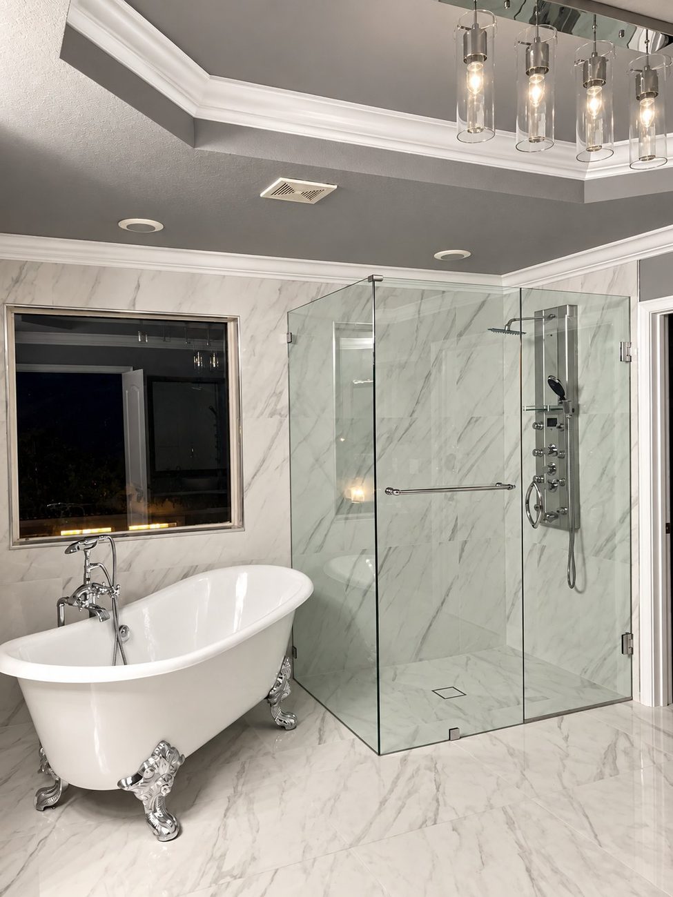 Frameless glass corner shower enclosure with shower panel beside a clawfoot tub
