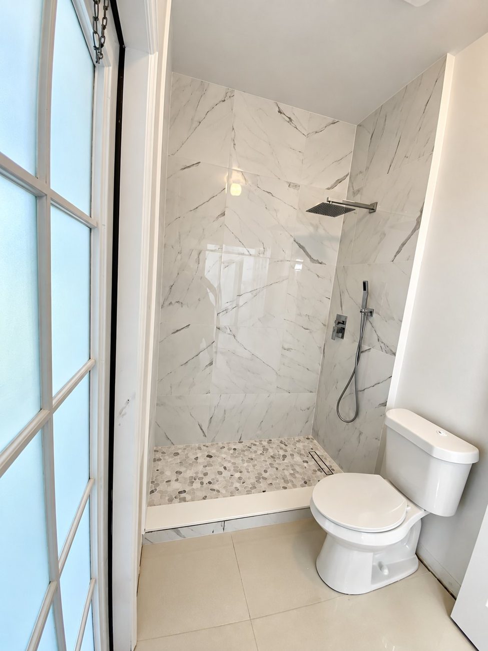 Shower with book-matched large-format porcelain walls and pebble mosaic floor