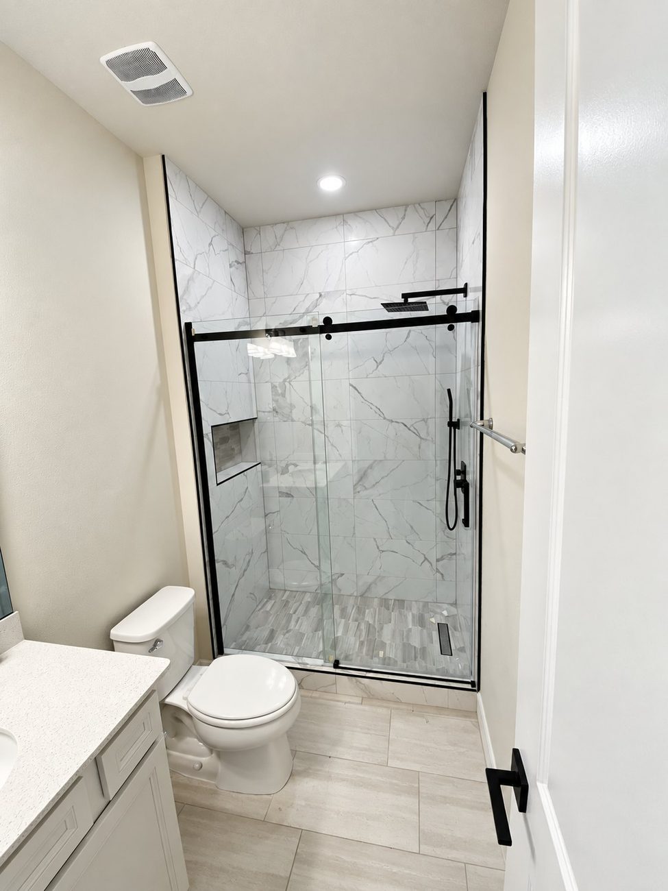 Shower with large-format porcelain walls, recessed niche and matte black framed sliding door