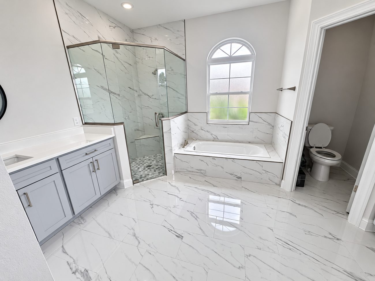 Neo-angle glass shower with a built-in seat and mosaic pan beside a drop-in tub set into a tiled deck