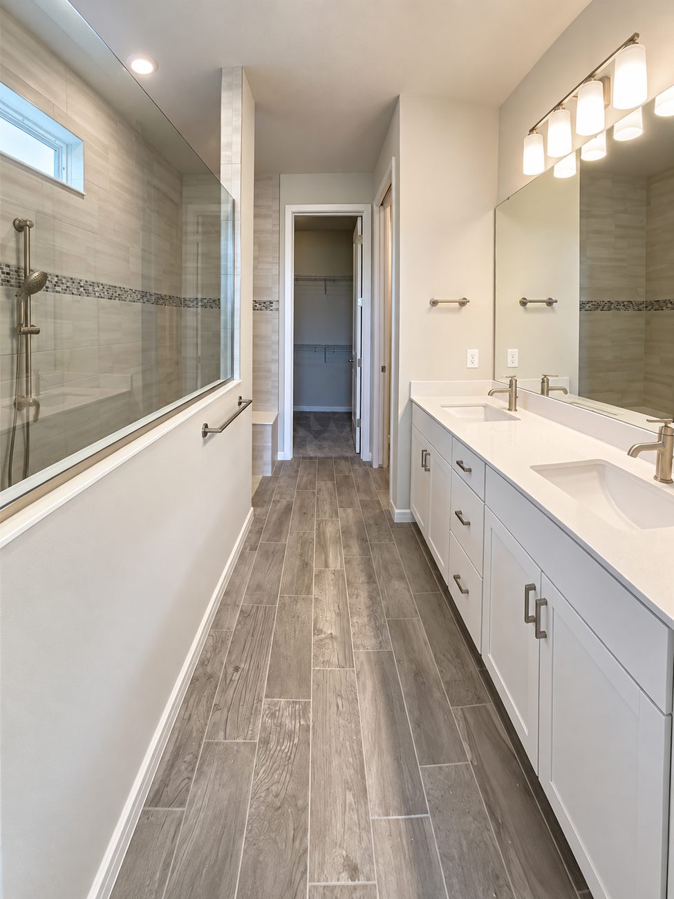 Long bathroom with a walk-in shower behind a glass half-wall, mosaic accent band, double quartz vanity and wood-look plank floor