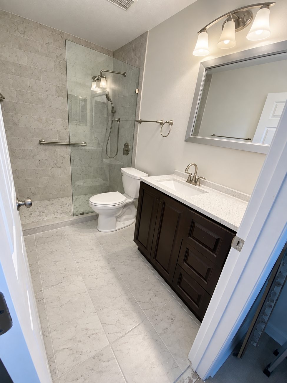 Walk-in shower behind a frameless glass panel with a grab bar, marble-look wall tile and mosaic pan, espresso vanity with a quartz top and marble-look floor tile