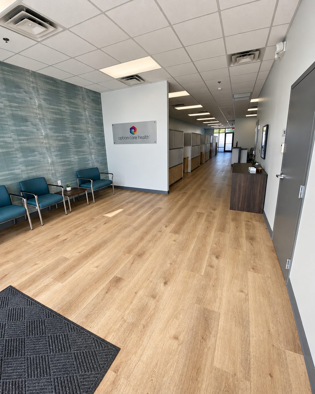Office reception with teal waiting chairs, textured feature wall and light plank flooring