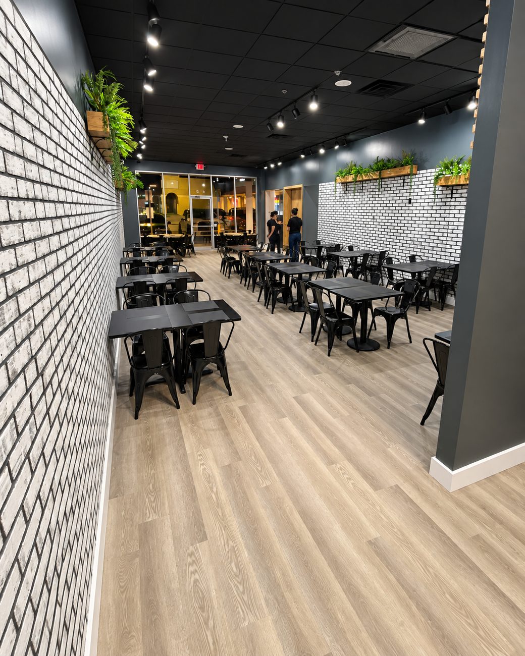 Restaurant dining room with black ceiling, track lighting, white painted brick wall and black tables