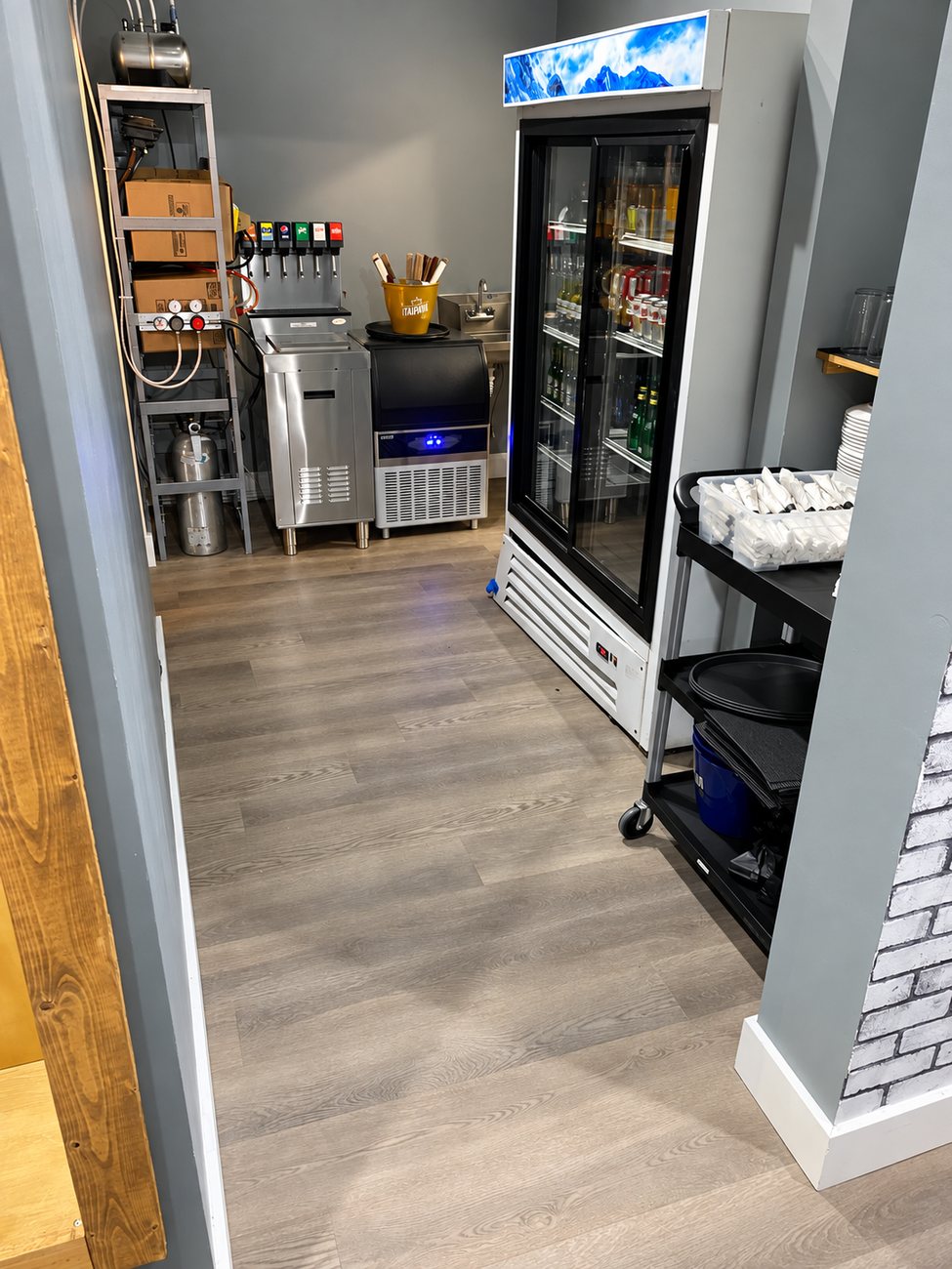 Restaurant service area with a soda fountain tower, ice machine, glass-door beverage cooler and grey plank flooring