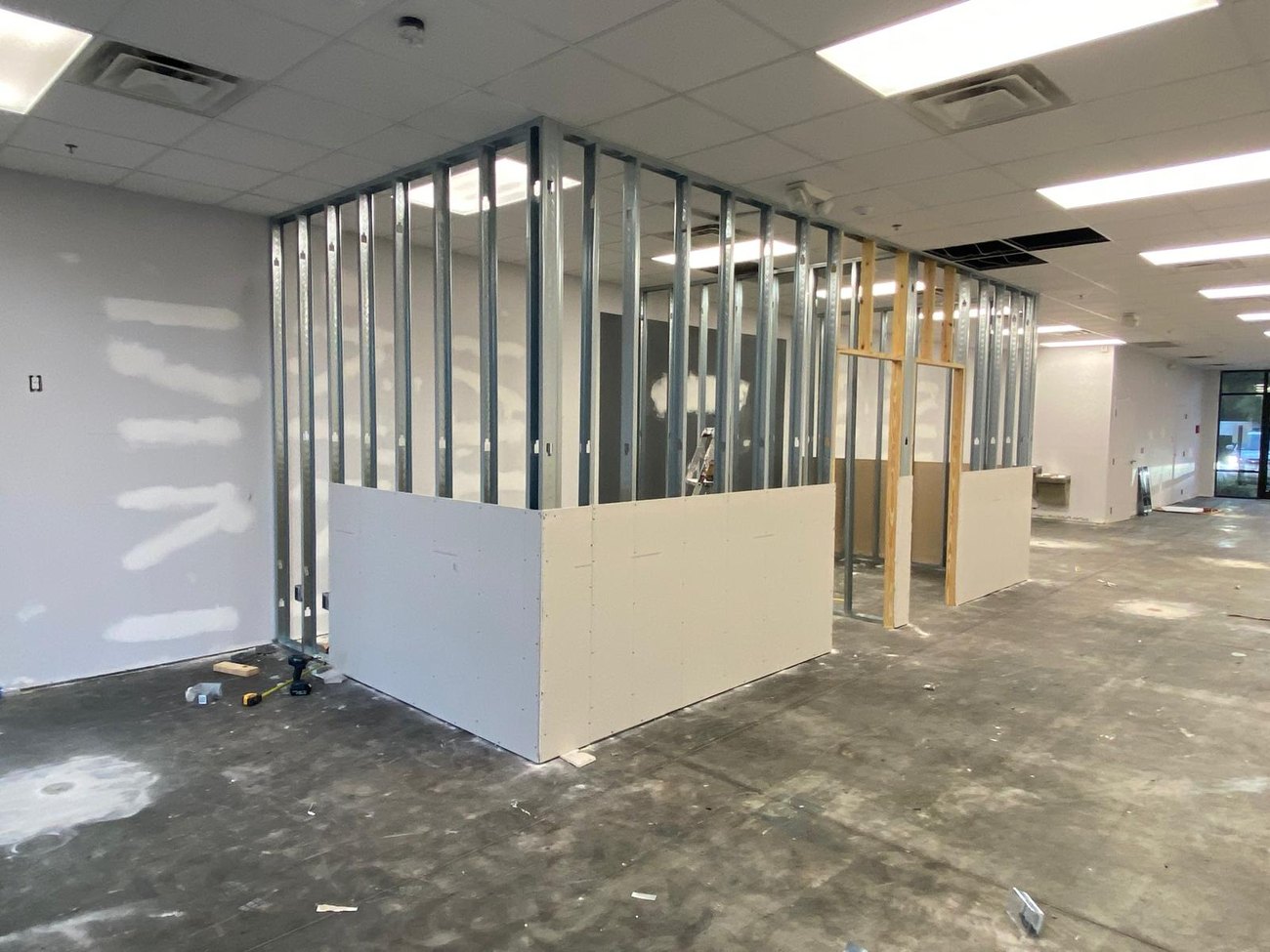 Commercial unit mid build-out with steel stud partition walls, drywall hung to half height and a bare concrete floor