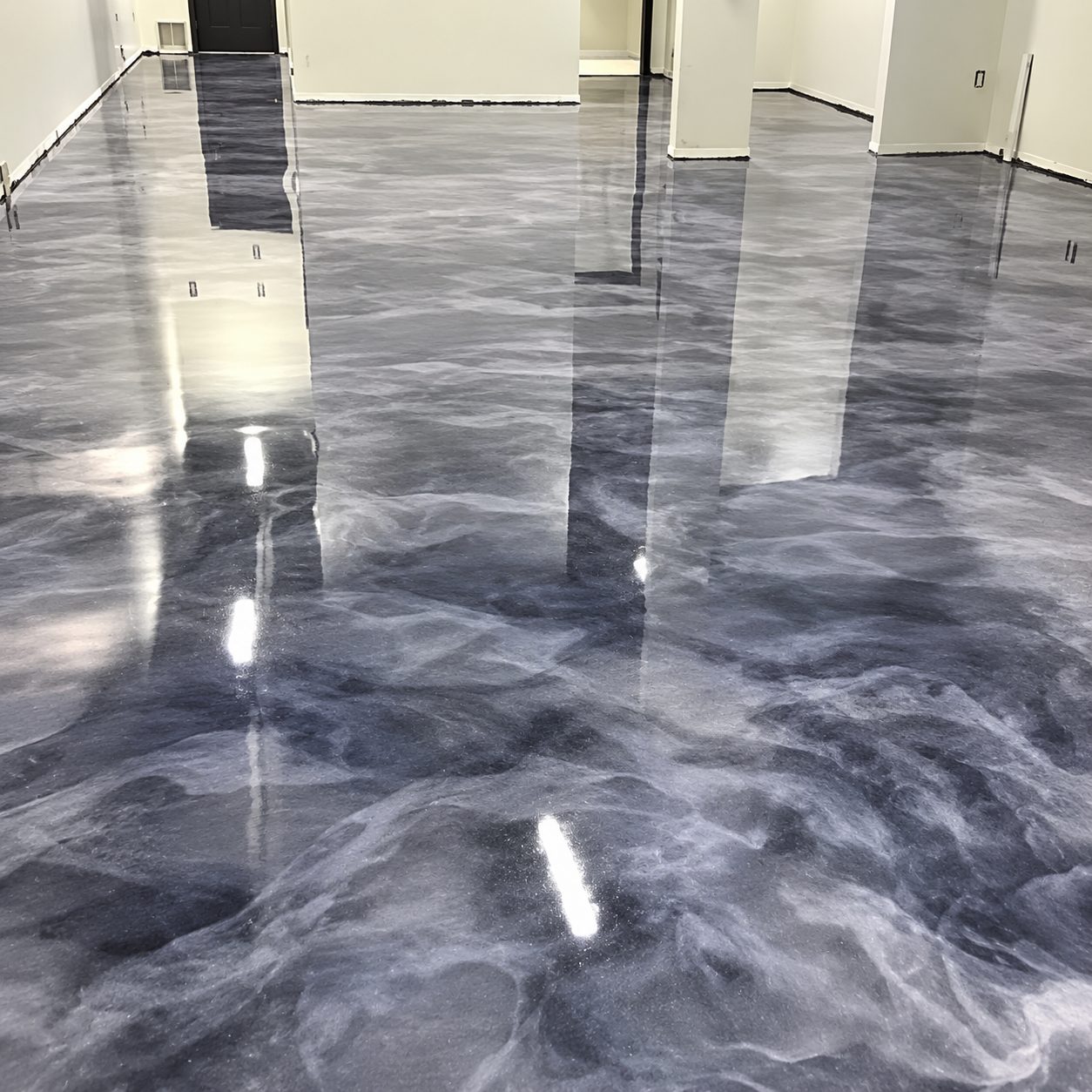 Blue-grey metallic epoxy floor in an open commercial space reflecting the columns