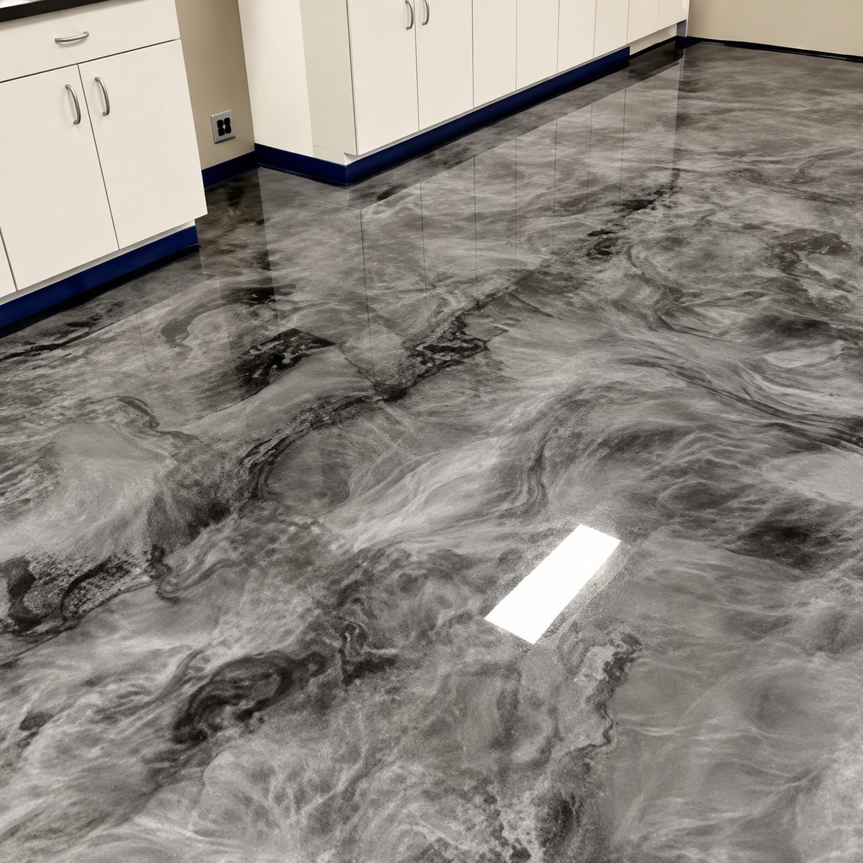 Grey and white metallic epoxy floor finished up to a blue cove base beneath cabinets
