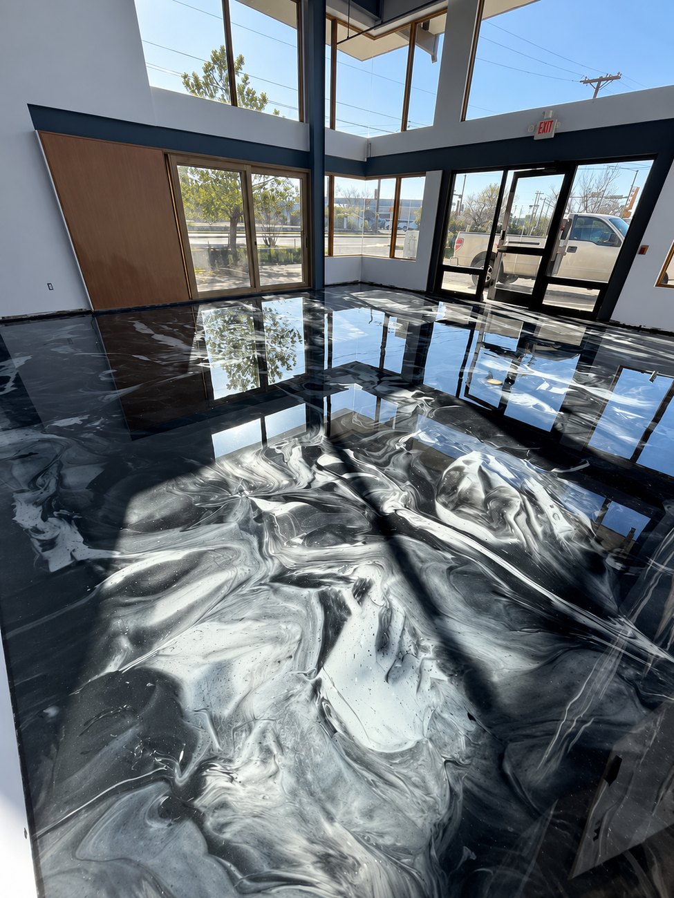 Black and white metallic epoxy floor in a glass-fronted commercial lobby, reflecting the windows
