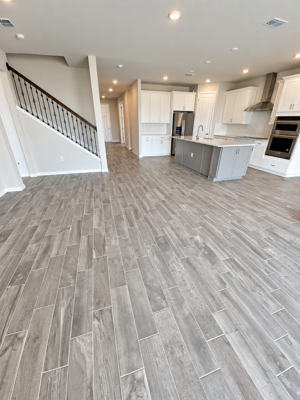 Grey wood-look plank tile running through an open plan from the stair landing to the kitchen