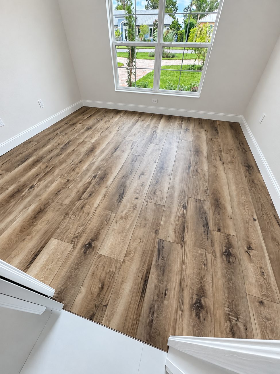 Wide-plank flooring in a room with a tall window, meeting the tile floor at a flush transition in the doorway