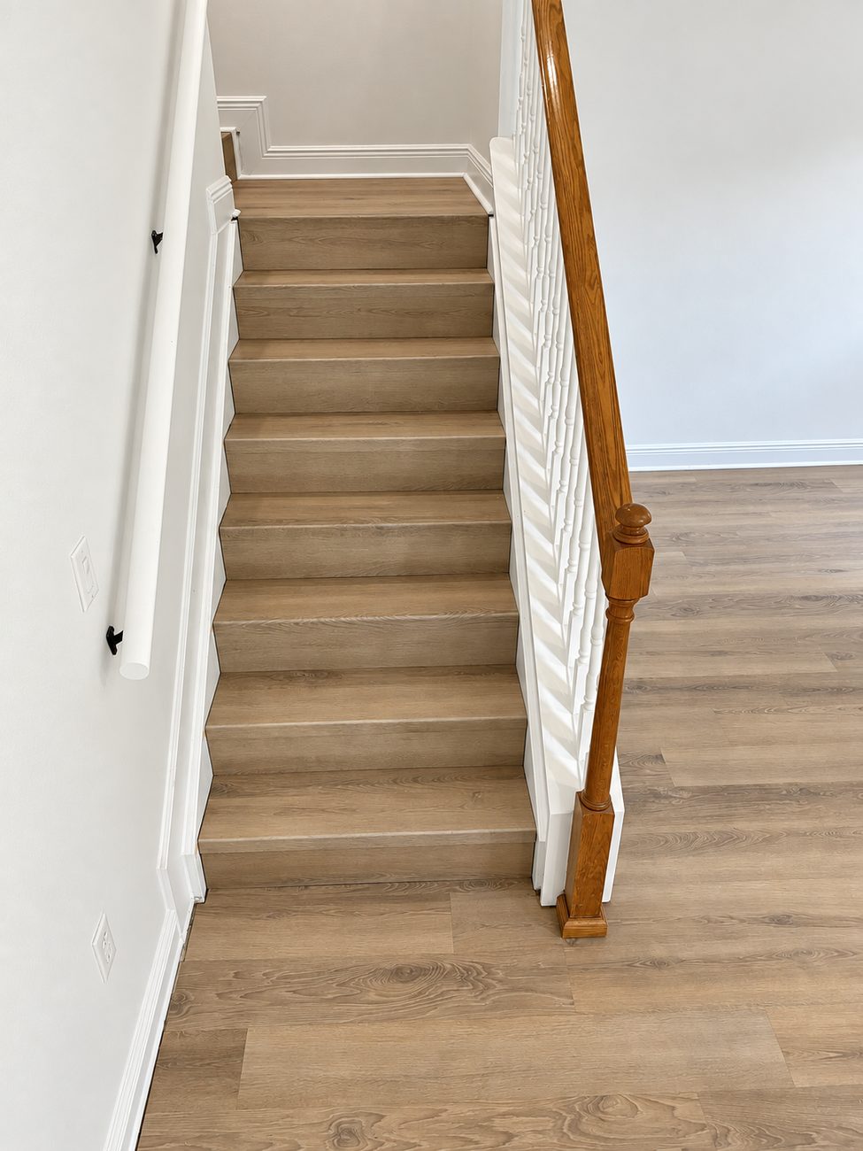 Stair treads finished to match the plank floor at the landing, with painted white risers and an oak handrail
