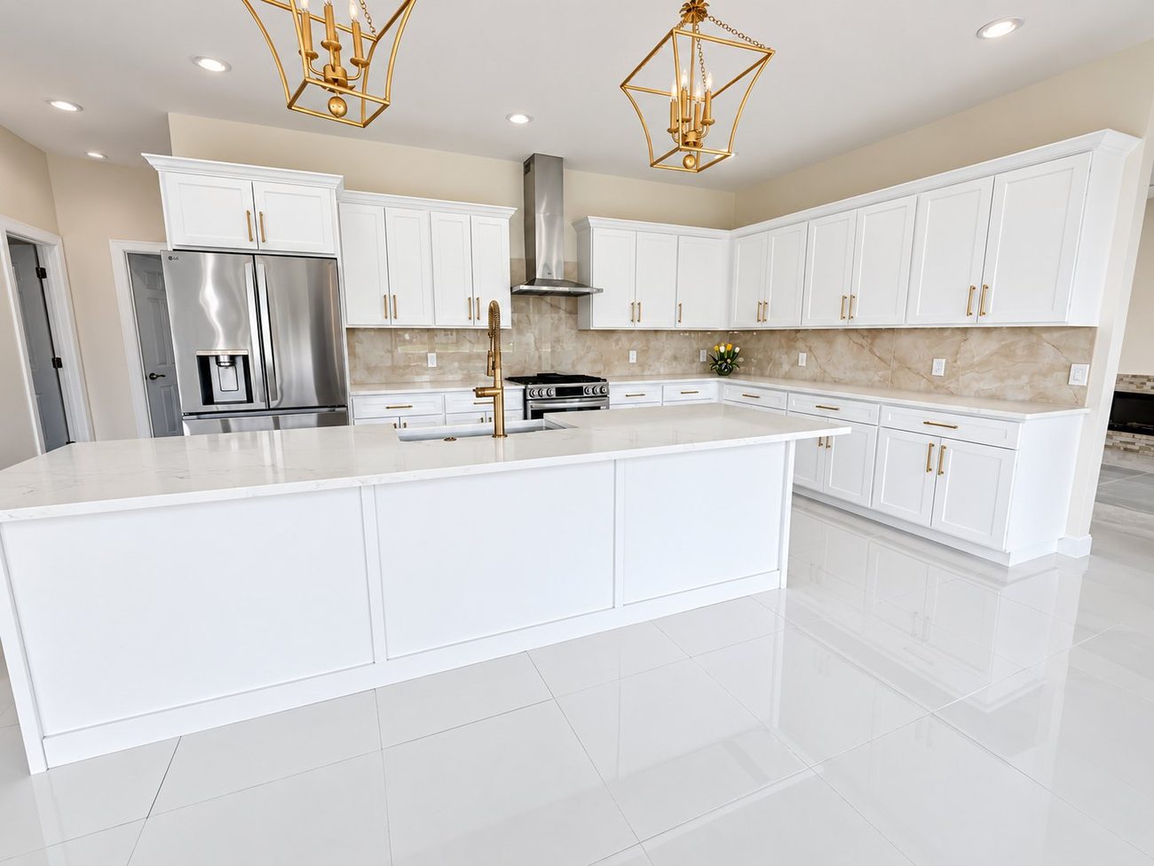 White kitchen with gold hardware, lantern pendants and a long marble-look quartz island