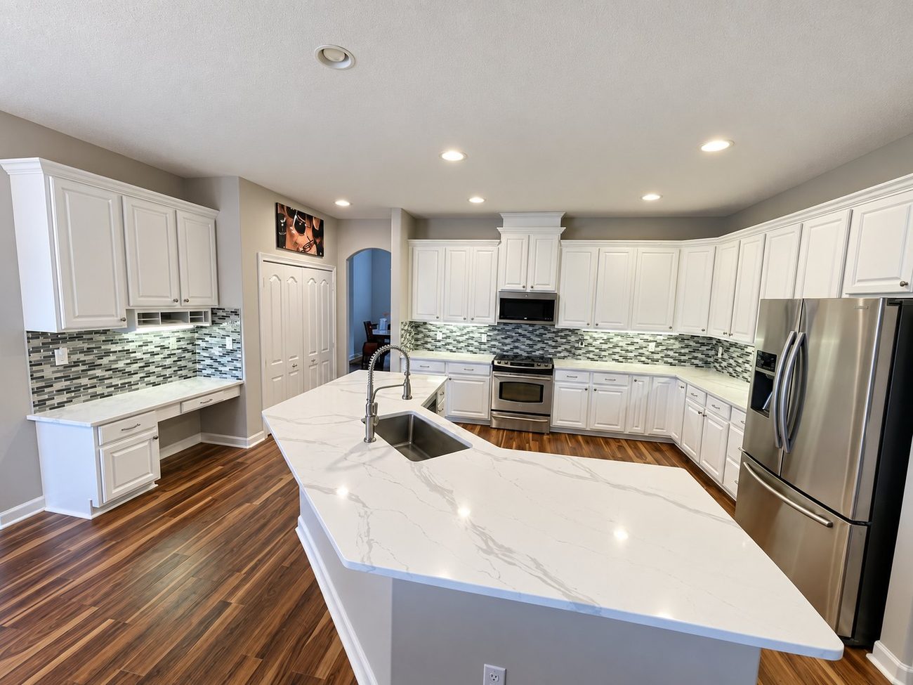 Kitchen with large angled quartz island, glass mosaic backsplash and a built-in desk area