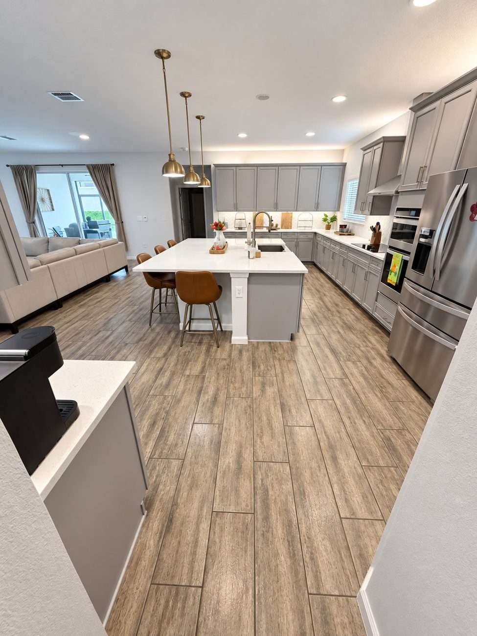 Grey kitchen with white quartz island and gold pendants, open to the living room