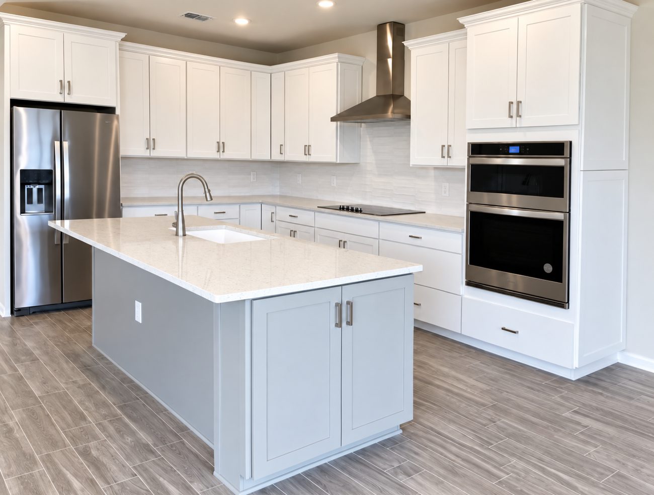 White shaker kitchen with a quartz island, stacked wall ovens, stainless hood and wood-look plank tile floor