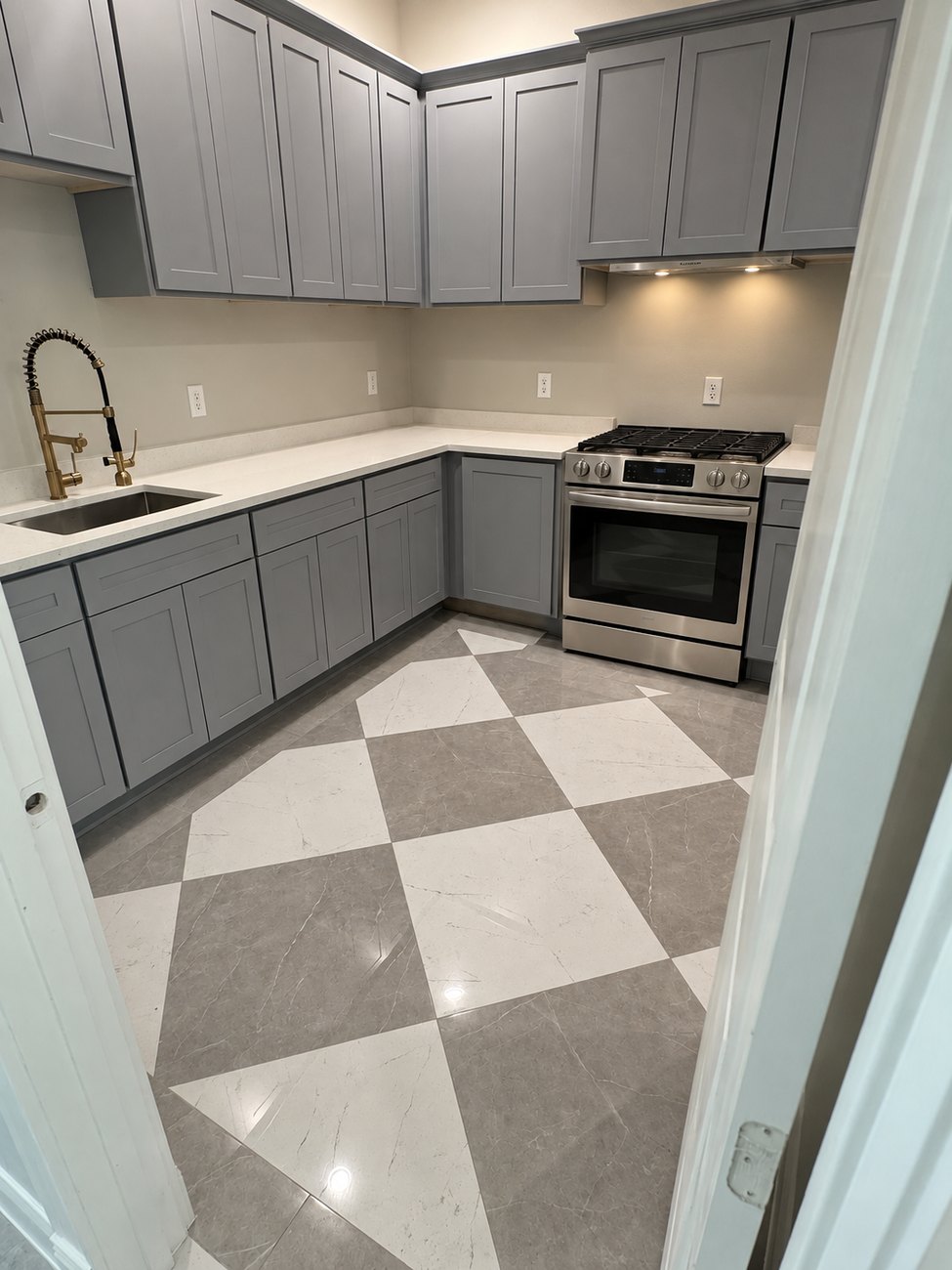 Galley kitchen with grey shaker cabinets, quartz counters, a gas range and a diagonal grey and white checkerboard tile floor