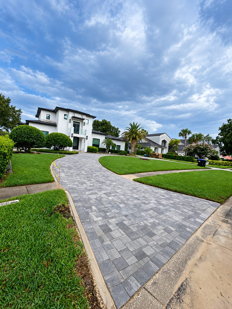 Long curved grey paver driveway leading to a modern white house