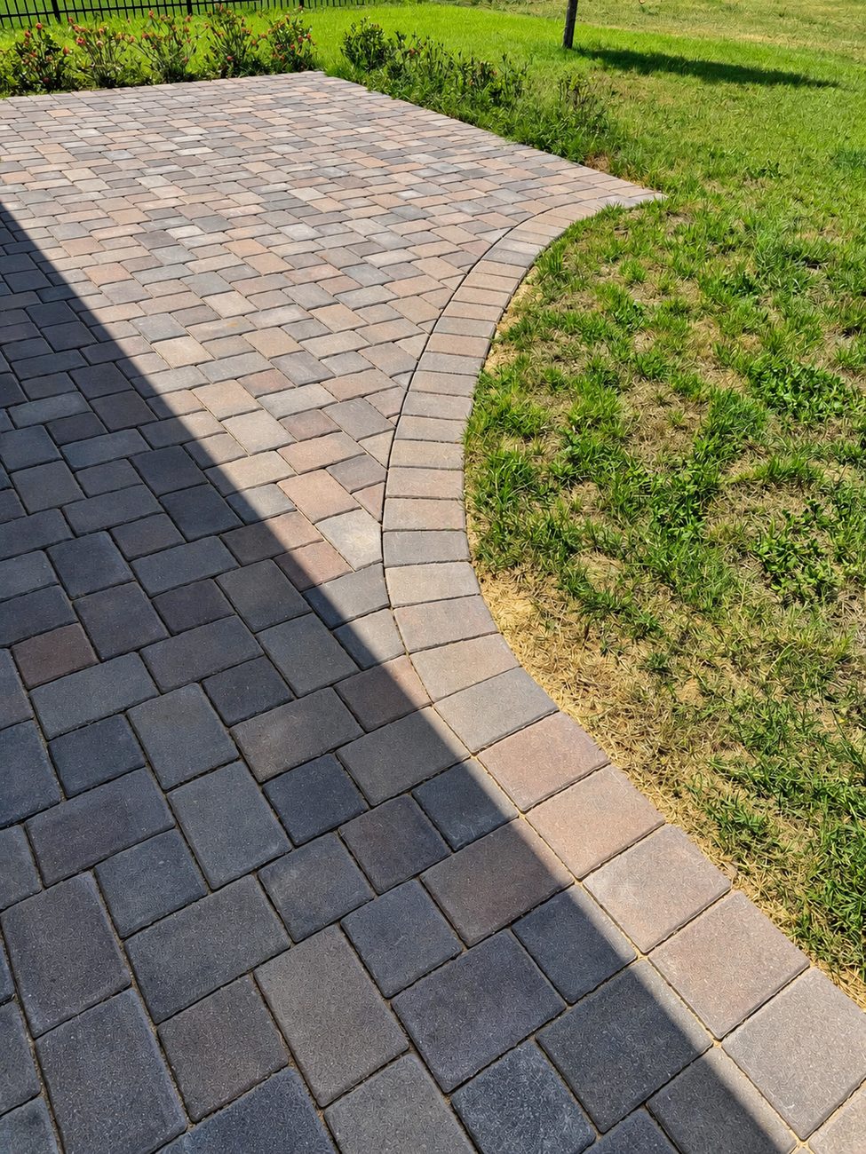 Close view of a curved paver border course where charcoal pavers meet a tan soldier course at the lawn edge