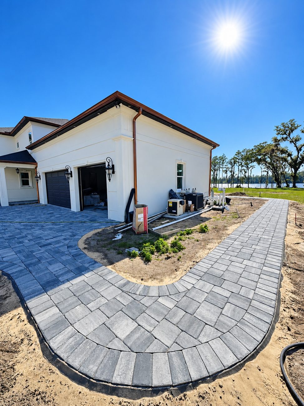 Curved paver walkway running along a new house under construction toward a lake