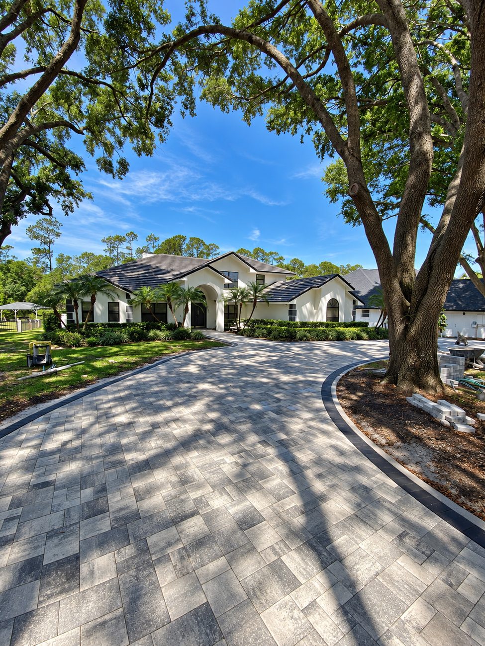 Long curved paver driveway with a charcoal edge band sweeping up to the entry of a house under live oaks
