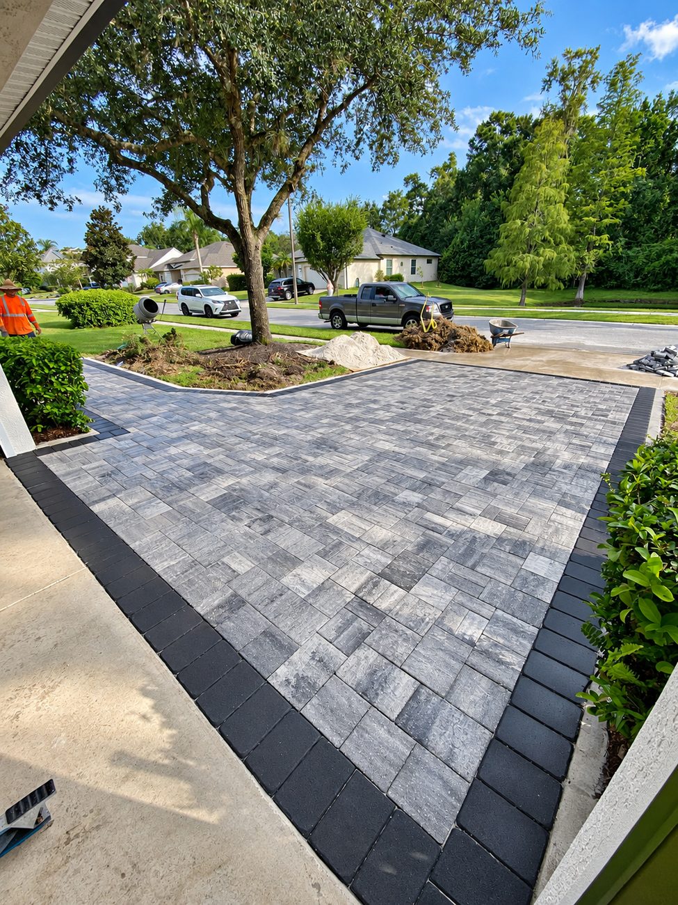 Grey paver driveway framed by a charcoal border, photographed from the front porch while the job was still underway