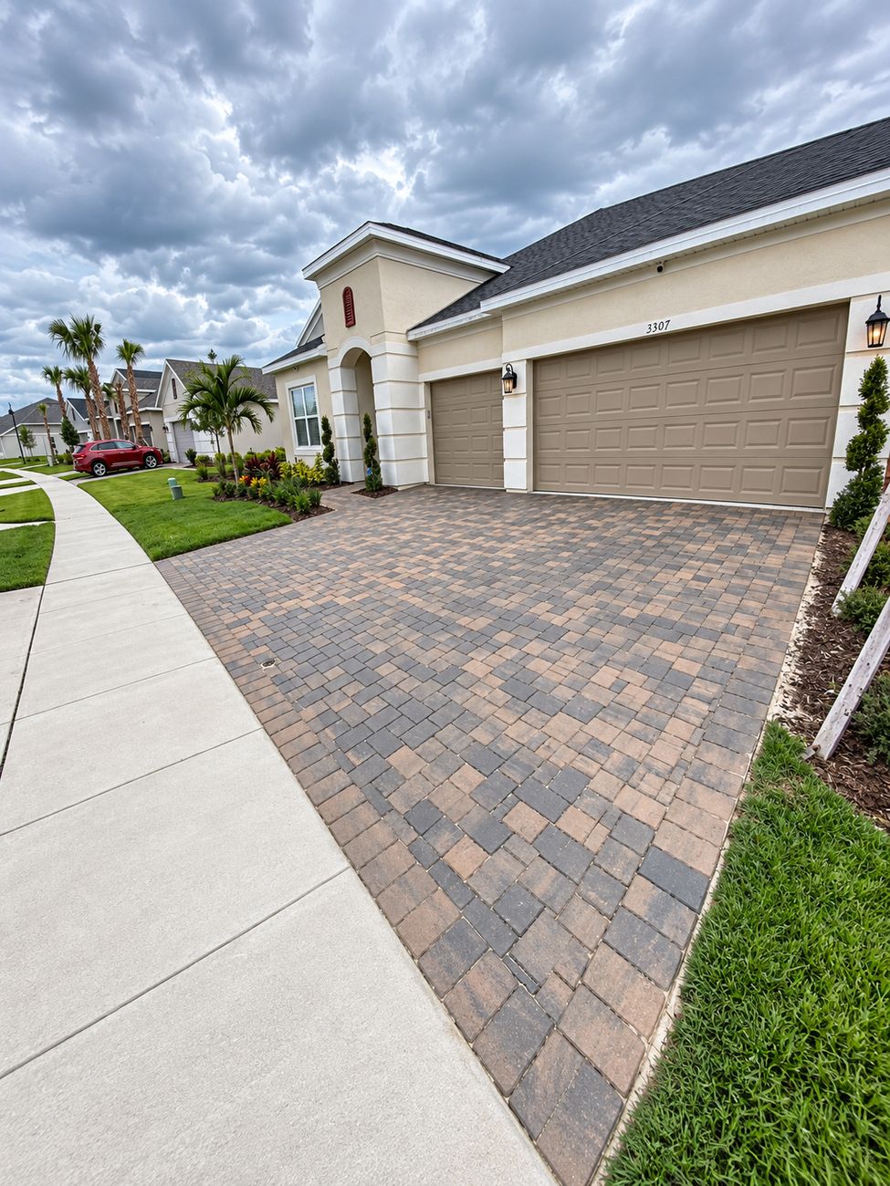 Tan and charcoal paver driveway laid up to a three-car garage, edged where it meets the public sidewalk
