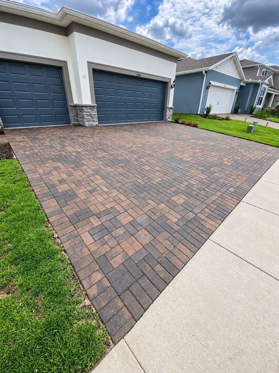 Brown and charcoal paver driveway running the full width of a three-car garage with stone columns