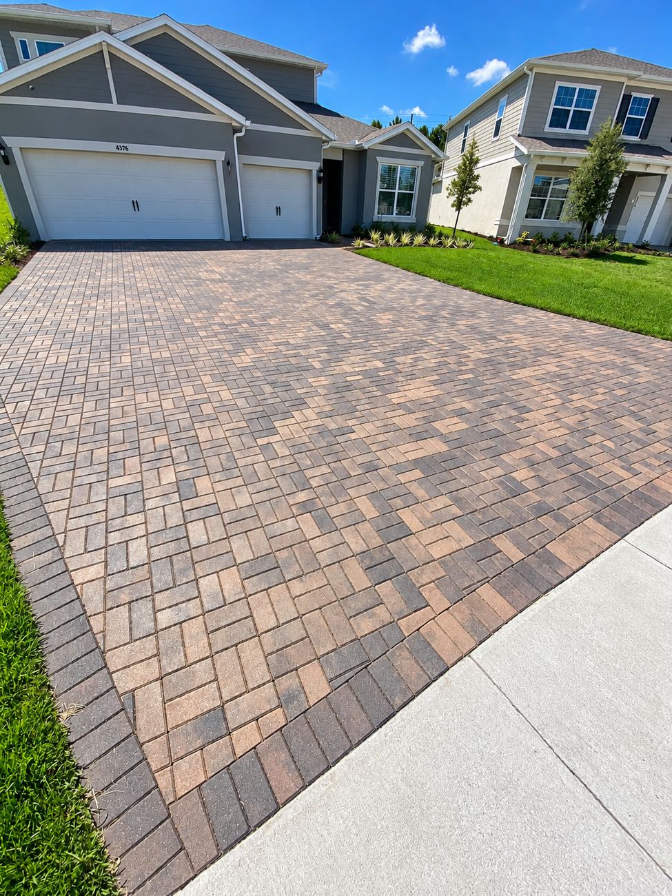 Wide tan paver driveway with a darker border course framing it on both sides
