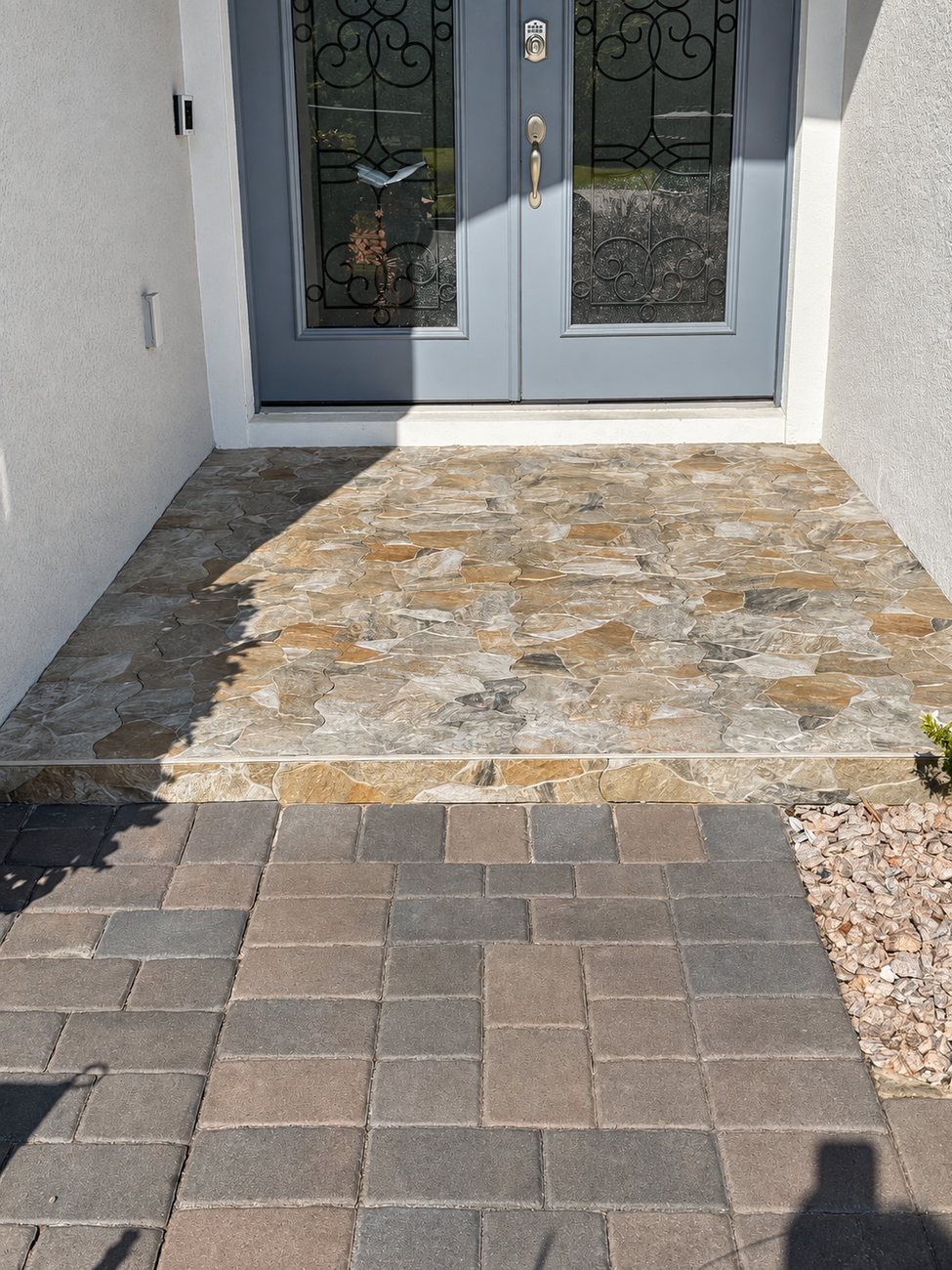 Irregular tan and grey flagstone landing at a double front door, meeting a paver walkway at the step below