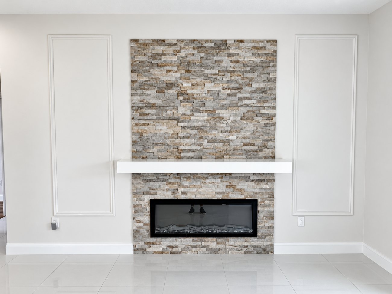 Stacked stone ledger panel running floor to ceiling behind a linear fireplace with a white floating mantel